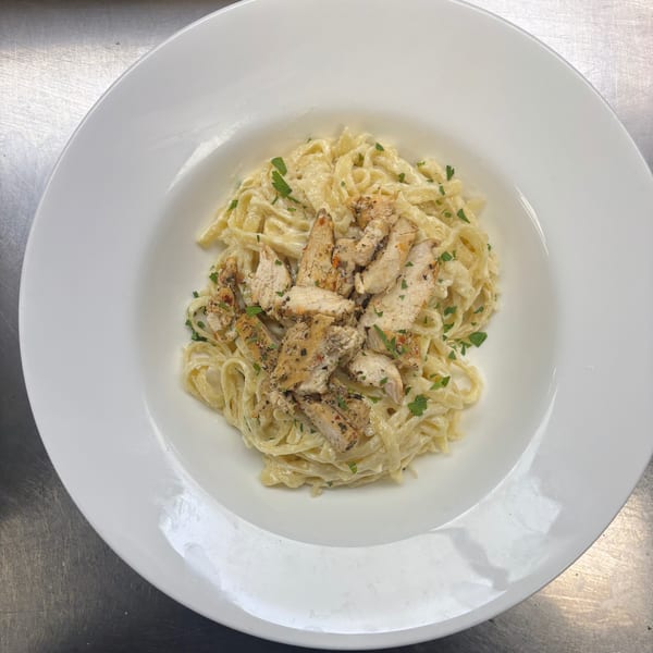 Creamy fettuccine alfredo with grilled chicken and parsley in a white bowl.