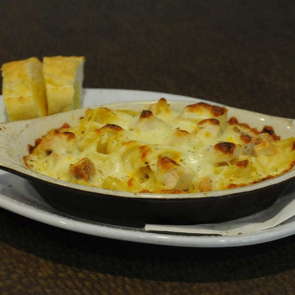 Baked pasta with melted cheese and chicken in a white dish, served with two slices of bread.