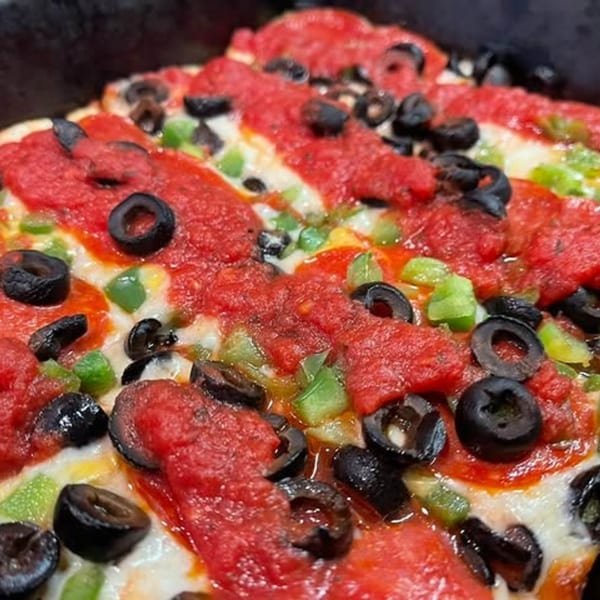 Close-up of a Junct'n Square Pizza with red sauce, melted cheese, black olives, and green peppers.