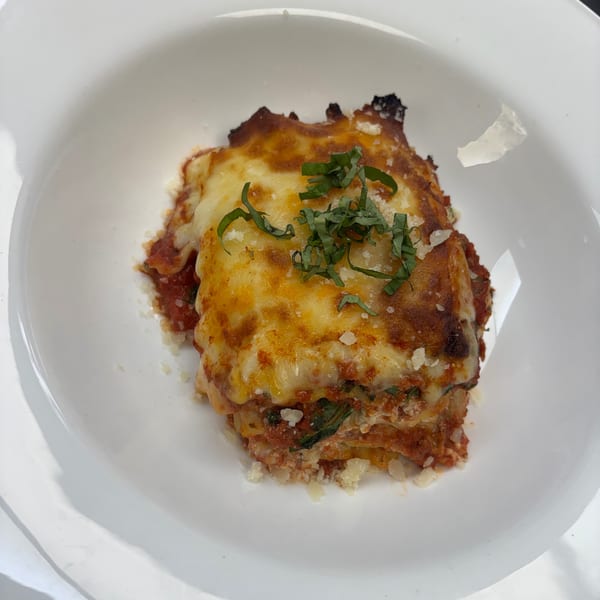 A serving of lasagna with melted cheese, tomato sauce, and fresh basil in a white bowl.