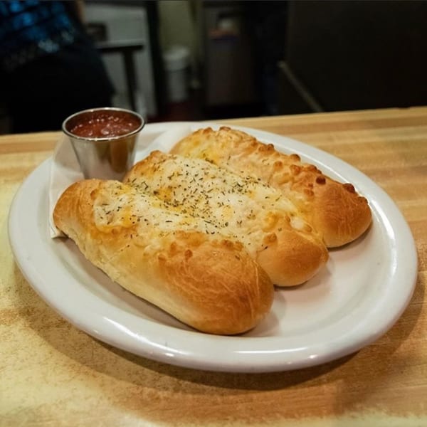 Three golden-brown breadsticks topped with herbs and cheese, served with a side of marinara sauce.