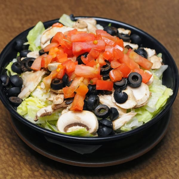 A black bowl of Junct'n Square Pizza salad with lettuce, mushrooms, black olives, and diced tomatoes.