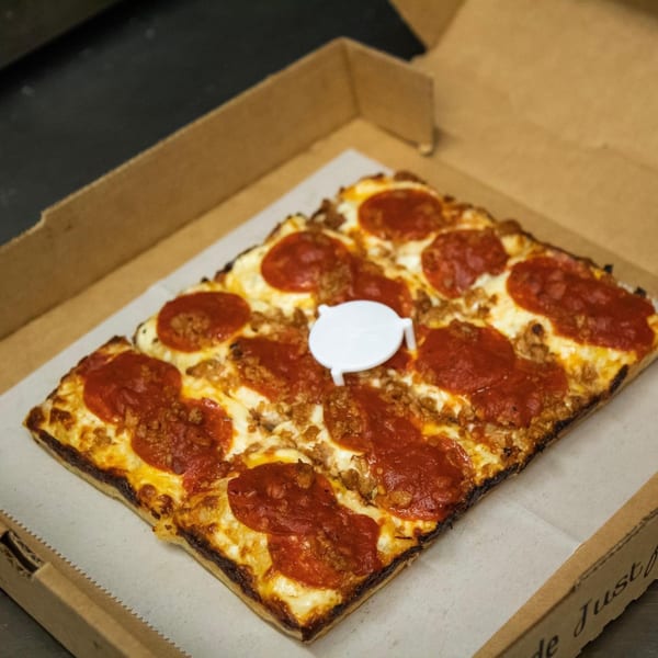 A square Junct'n Square Pizza with pepperoni and sausage in a cardboard box.