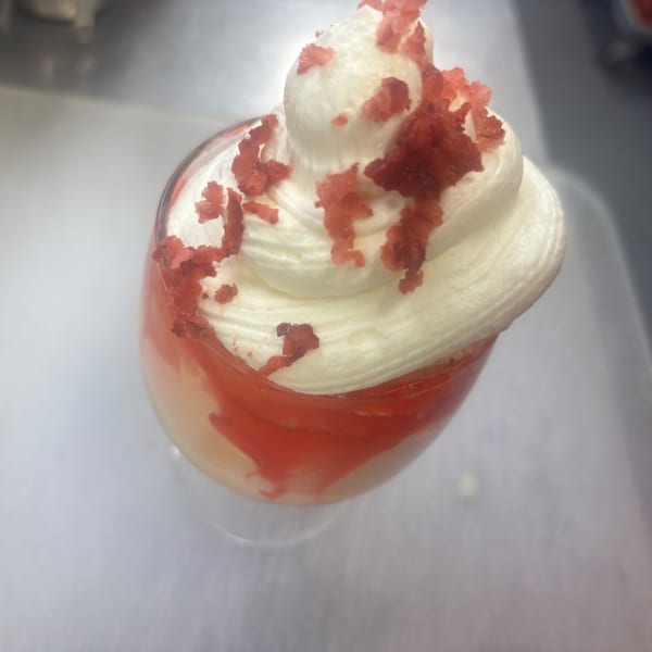A glass of red velvet dessert with white whipped cream and red crumbs on top.