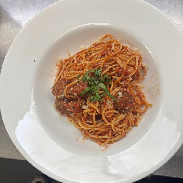 Spaghetti and meatballs with tomato sauce, parmesan cheese, and fresh basil in a white bowl.