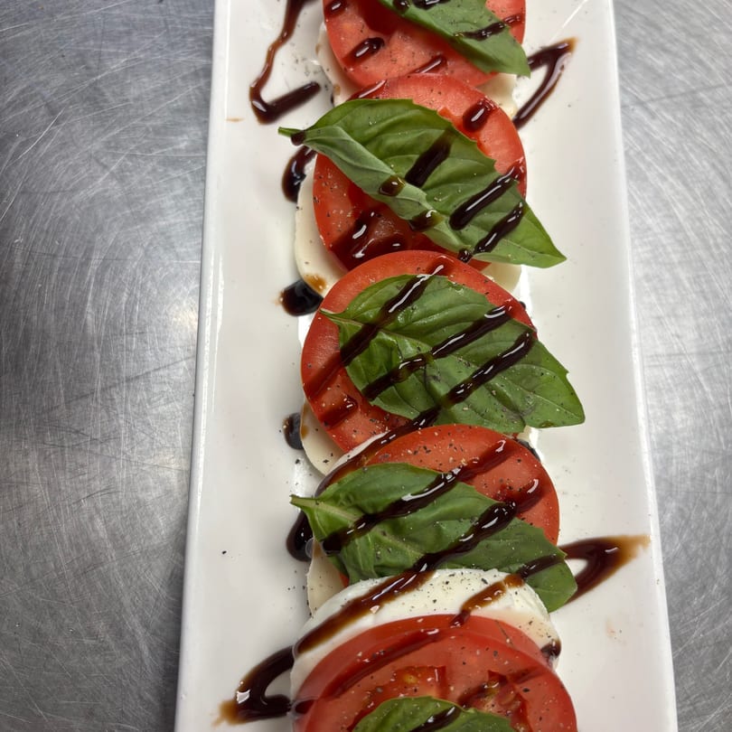 Fresh Caprese salad with tomatoes, mozzarella, basil, and balsamic glaze on a white rectangular plate.
